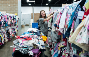 A  female shopper smiles at the camera with a wagon full of clothing she has already found.